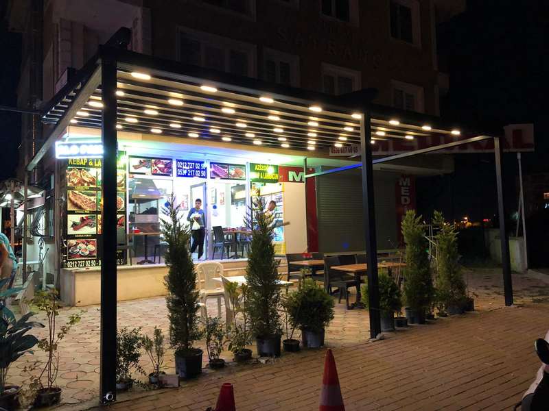 İstanbul'da bir işletmenin önüne kurulan koyu renkli pergola; LED aydınlatmalı çatı akşam saatinde vitrini ve dış oturma alanını aydınlatıyor