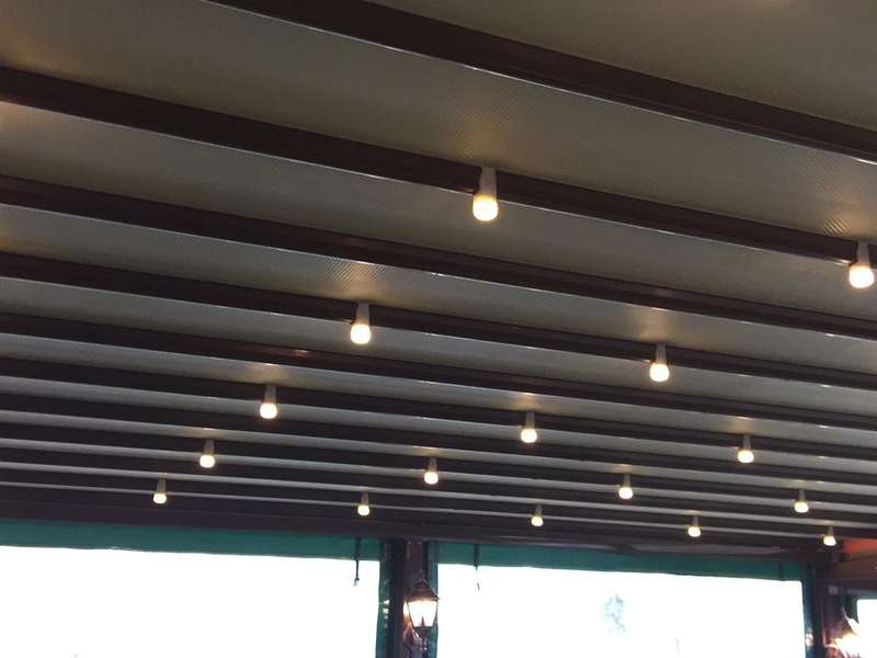 Kahverengi lamelli pergola çatısının alttan görünümü; kirişler arasına yerleştirilmiş sarkıt aydınlatmalar