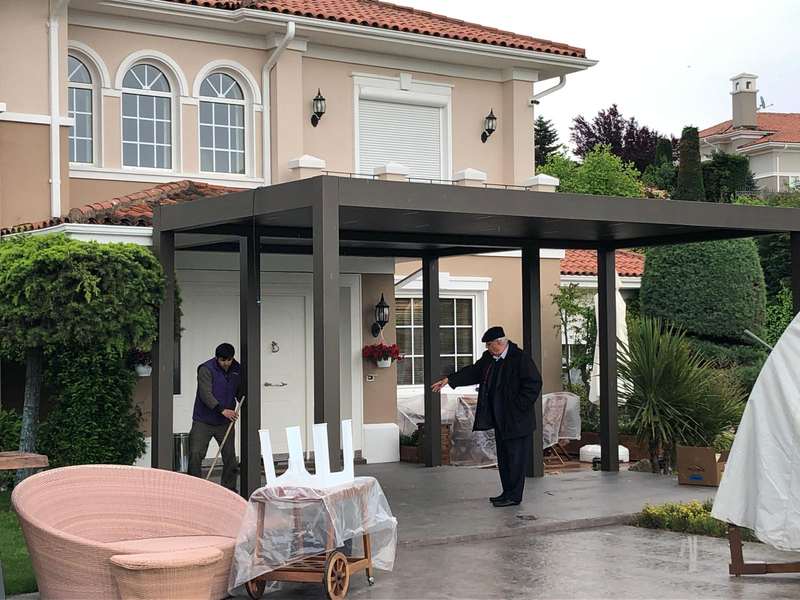 Kemerli pencereli villanın girişine kurulan antrasit bioklimatik pergola; montaj sonrası temizlik yapılıyor