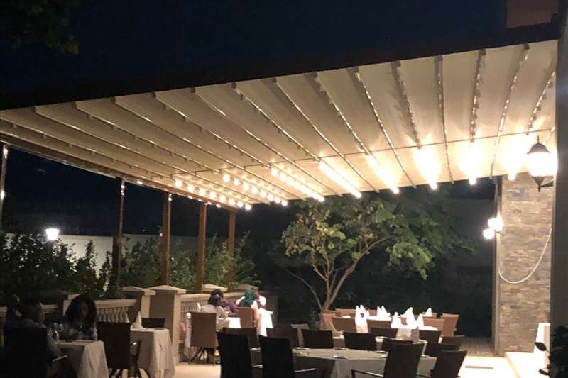 Akşam saatinde restoran terasını örten LED aydınlatmalı beyaz alüminyum pergola