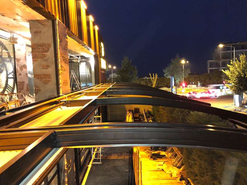 Gece çekilmiş tonozlu cam kapatma sistemi; sarı iç aydınlatma tuğla duvarı yansıtıyor, dışarıda yol ışıkları
