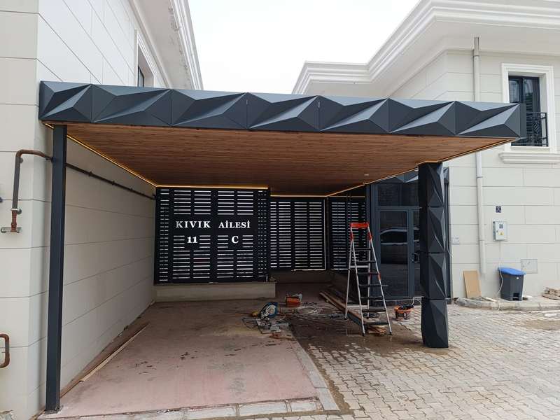 Villa girişine kurulan araç gölgeliğinin montaj aşaması; alınlıkta üç boyutlu kırılımlı antrasit kompozit panel, tavanda ahşap desenli kaplama ve LED şerit, arkada lazer kesim desenli bahçe kapısı