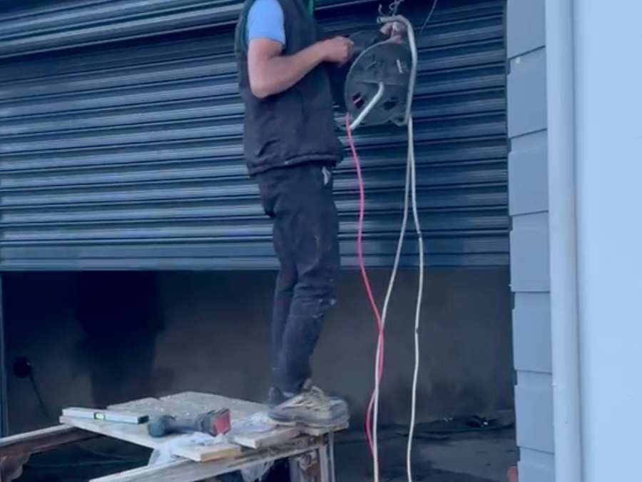 Garaj girişine kurulan motorlu sarmal kepenk; montaj aşamasında usta üst kutuya elektrik bağlantısını çekiyor, üstte çelik taşıyıcı kirişler görünüyor