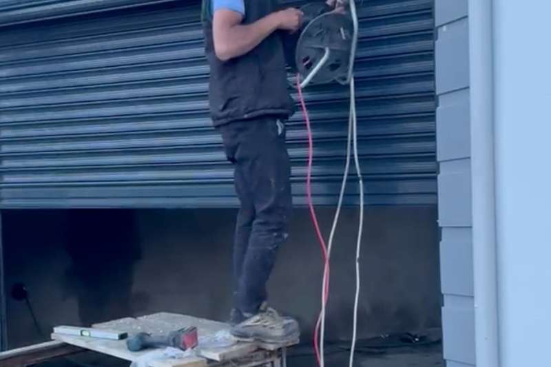 Garaj girişine kurulan motorlu sarmal kepenk; montaj aşamasında usta üst kutuya elektrik bağlantısını çekiyor, üstte çelik taşıyıcı kirişler görünüyor