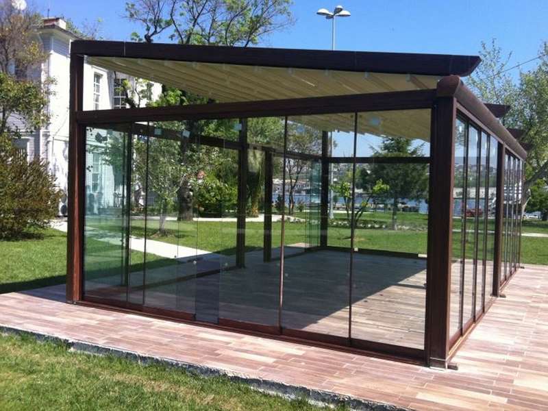 Geniş yeşil bahçe içinde ahşap deck üzerine kurulmuş kahverengi doğramalı, dört cephesi cam kış bahçesi