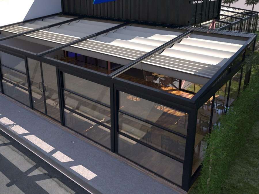 Antrasit pergola ve giyotin cam sisteminin üstten görünümü; kısmen açık lameller arasından gökyüzü ve arka planda yerleşim görünüyor