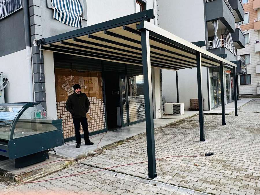 Tunceli'deki market önü pergolanın yandan görünümü; taşıyıcı ayaklar kaldırıma yerleştirilmiş, çatı dükkân cephesine yaslanıyor