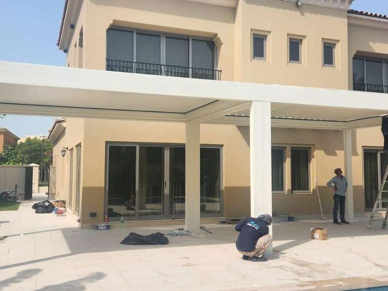 Villa cephesine kurulan beyaz bioklimatik pergolanın montaj aşaması; taşıyıcı kolonlar dikilmiş, ekip lamel montajı yapıyor