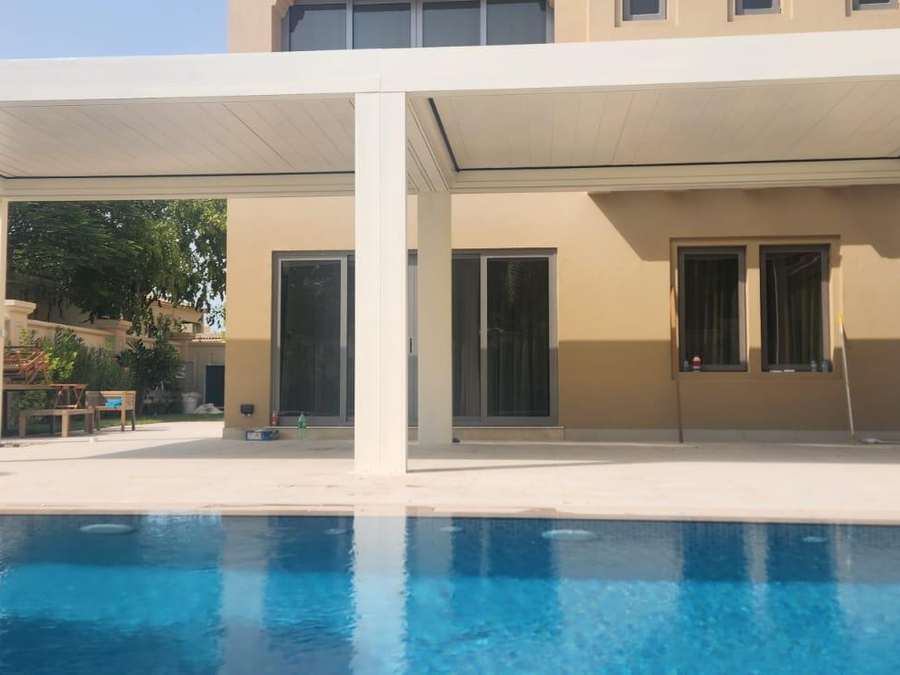 Villa havuz kenarındaki beyaz bioklimatik pergolanın tamamlanmış hâli; havuz boyunca uzanan gölgeli oturma alanı